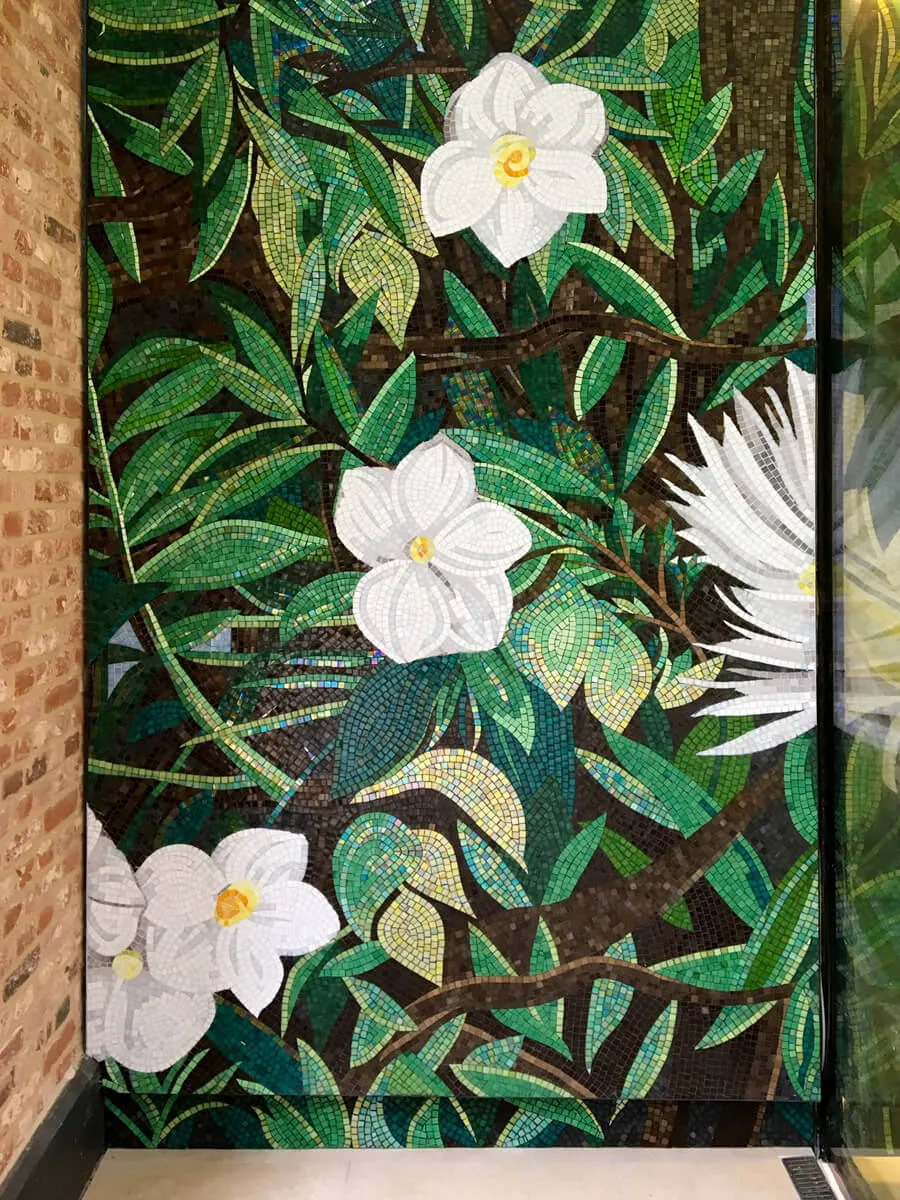 Wandmosaik mit weißen Blüten und grünen Blättern in einer Duschnische, die einzelnen Glassteine sind deutlich erkennbar.