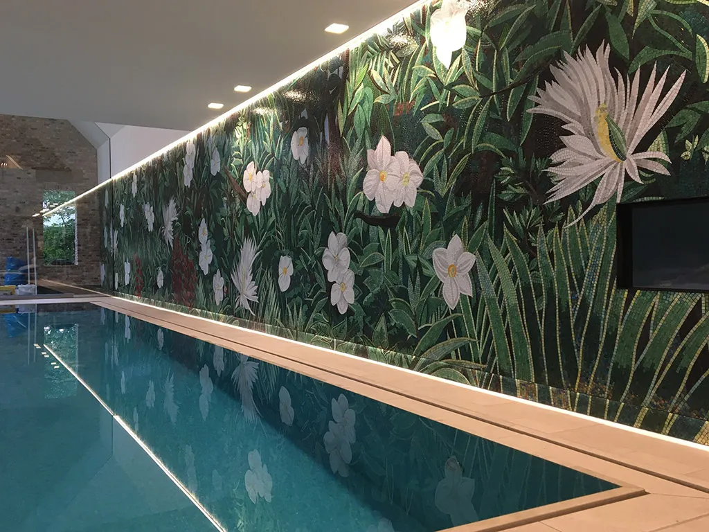 Blick entlang des Beckens auf das Wandmosaik, im Wasser spiegeln sich die weißen Blüten.