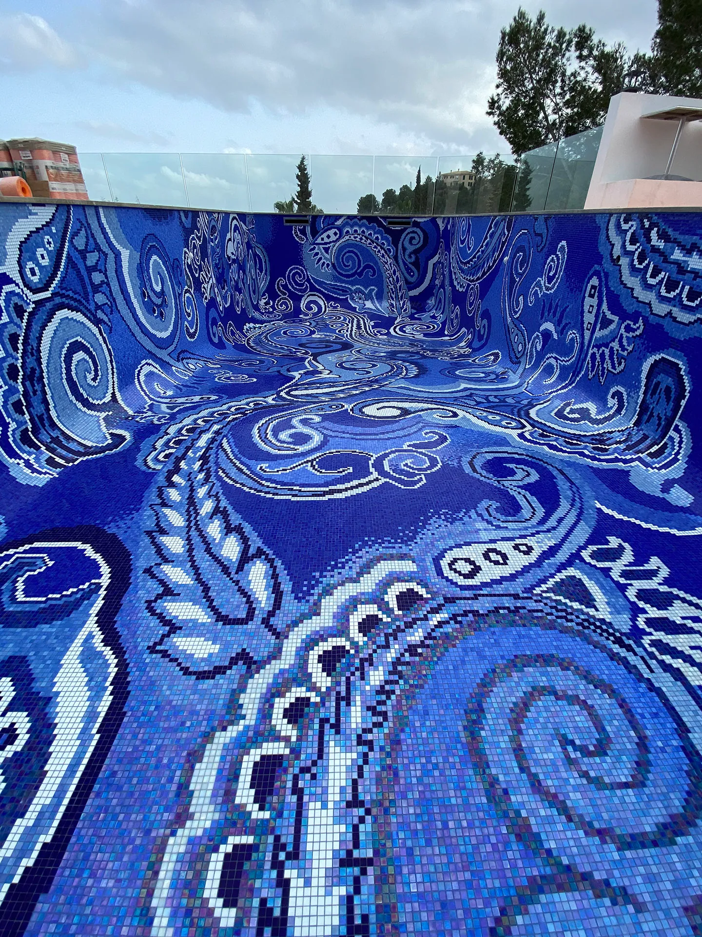Leeres Außenbecken, dessen Boden und Wände vollflächig mit einem blau-weißen Paisley-Ornament aus Glasmosaik belegt sind.